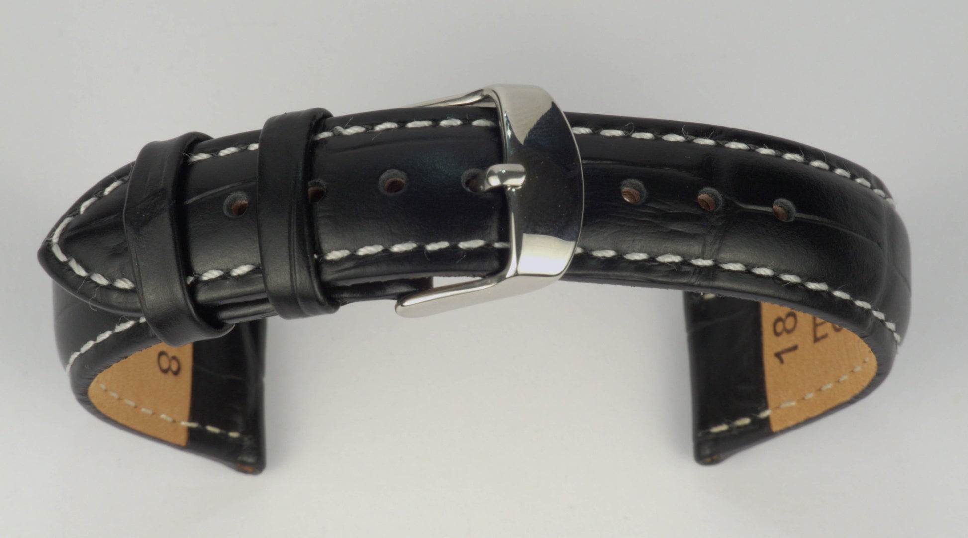 Lederuhrenarmband (Schwarz mit weißer Naht) zu einem Bogen geformt mit weißem Hintergrund. Detaillierte Nahaufnahme.